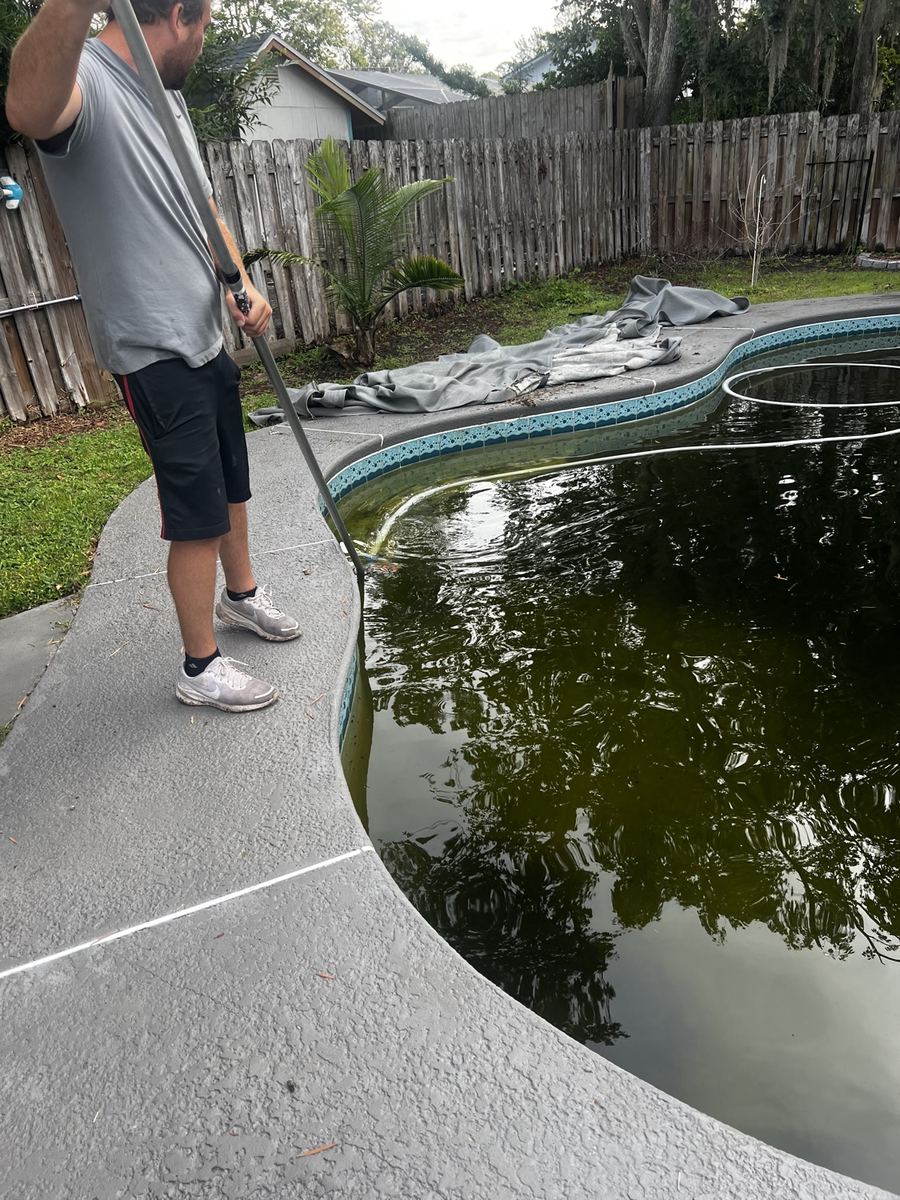 Pelican Pool and Patio technician vacuuming algae from a green swimming pool