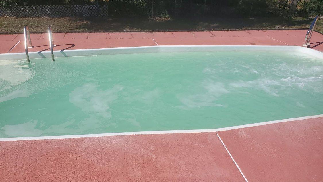 Same rectangular pool with cloudy light green water during treatment